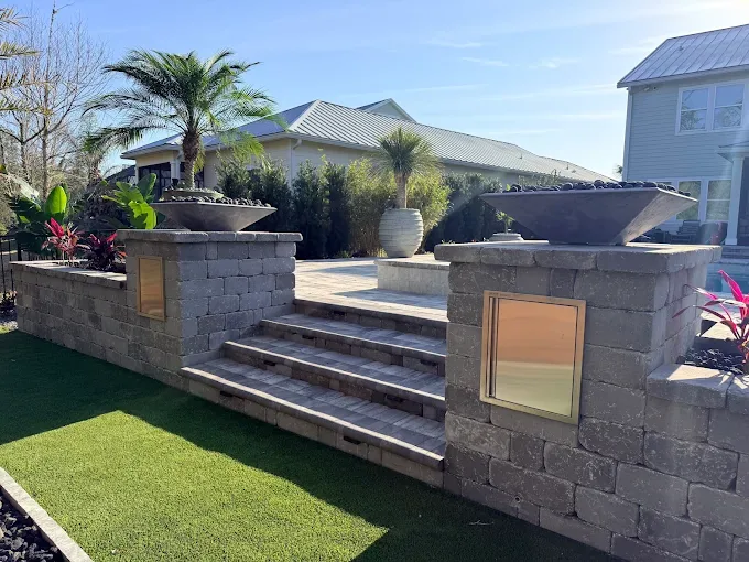 Raised paver steps with stone pillars topped by fire bowls and an artificial turf lawn in St. Augustine FL